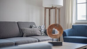 Una sala de estar con un sofá gris, un sillón azul, una lámpara de pie y un anillo decorativo de madera.