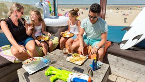 Un groupe de personnes est assis à une table en plein air, devant laquelle s’étend une vue sur la plage.