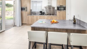 Eine moderne Küche mit einer zentralen Kochinsel, Holzschränken, einer Edelstahl-Dunstabzugshaube und einem Essbereich mit vier Stühlen.