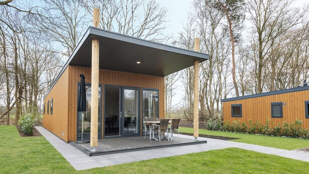 Eine moderne Holzhütte mit überdachter Terrasse, großen Schiebegläsern und einem Essbereich mit Gartenmöbeln.