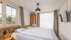 Een hotelkamer met een groot bed, nachtkastje, lamp, televisie aan de muur en een raam met gordijnen.