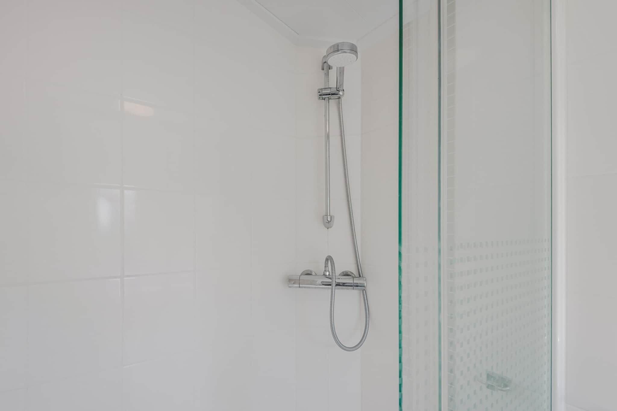 A shower with a handheld showerhead and a fixed showerhead, mounted on a wall with a glass door.