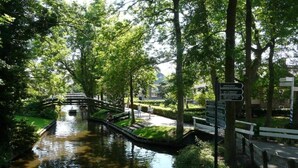 Un parque tranquilo con un estrecho canal de agua, un puente de madera y un cartel con indicaciones.