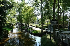 Un parque tranquilo con un estrecho canal de agua, un puente de madera y un cartel con indicaciones.