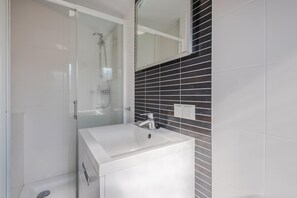 Ein modernes Badezimmer mit Duschkabine aus Glas, einem weißen Waschbecken und einer schwarzen gefliesten Rückwand.