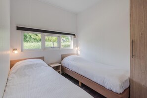 Ein Schlafzimmer mit zwei Einzelbetten, einem Nachttisch, einem Fenster mit Jalousien und einer Tür.
