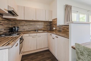 Une cuisine compacte avec des meubles de couleur bois clair, une cuisinière encastrée et un revêtement mural moderne.