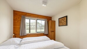 Een slaapkamer met een houten hoofdbord, een raam met gordijnen, een bed met wit beddengoed en een ingelijst beeld aan de muur.