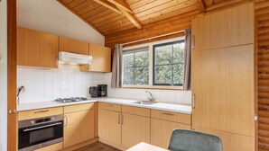 Een kleine keuken met houten kastjes, een gasfornuis, een spoelbak en een raam met gordijnen.