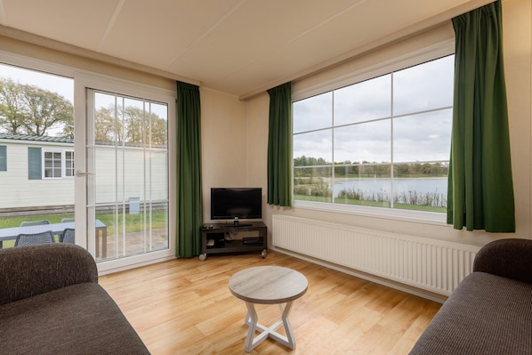 A living room with a TV, a round table, and a large window with curtains. - Charming Chalet in Borger (Borger)