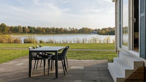 Un patio con tavolo e sedie affacciato su un lago, con un edificio sulla destra.