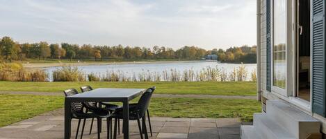 A patio with a table and chairs overlooking a lake, with a building on the right.