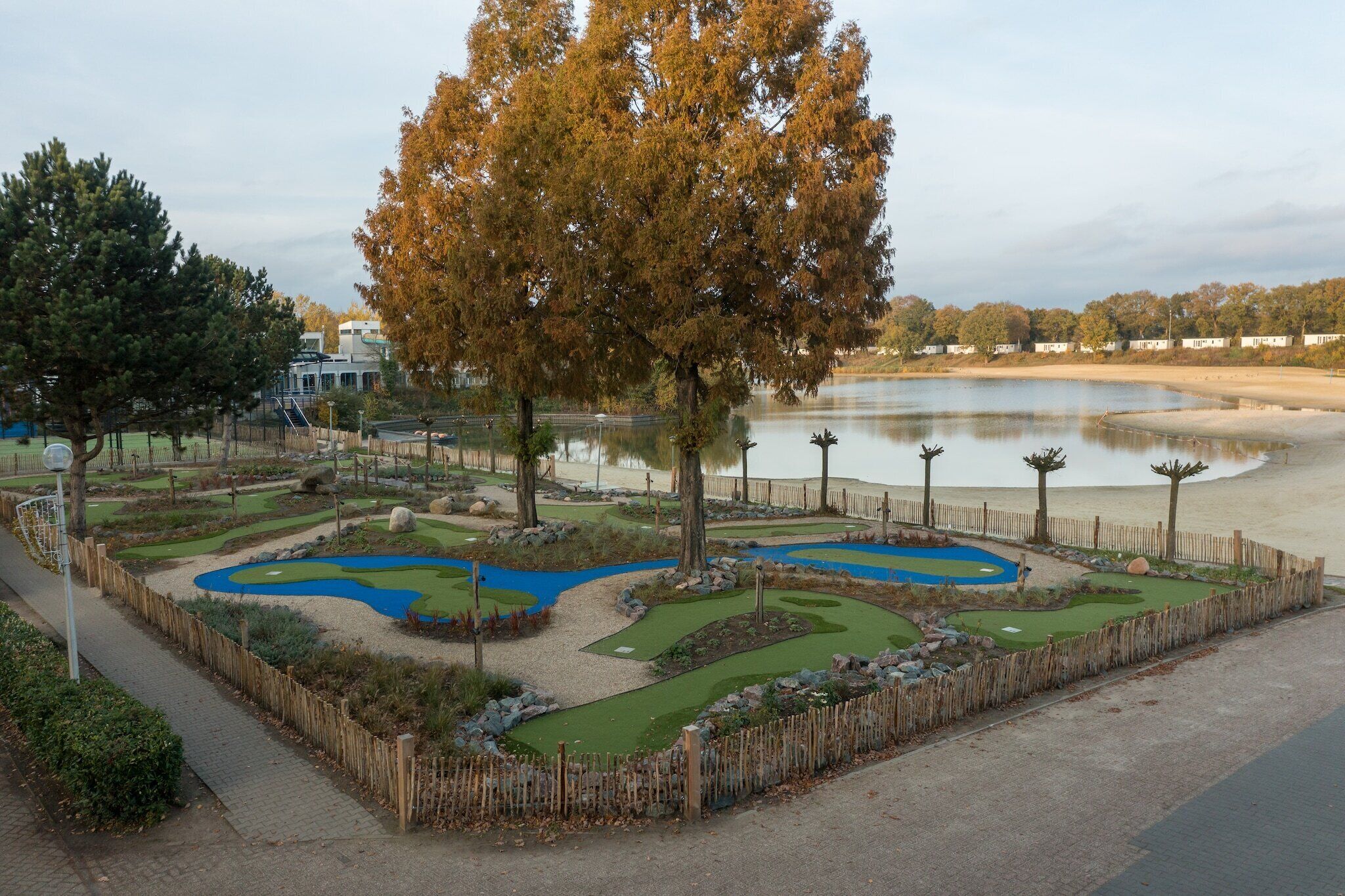 A miniature golf course with a pond, surrounded by trees and a wooden fence.