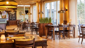 A restaurant with wooden tables and chairs, hanging pendant lights, and large windows with curtains. - Forest Glamping near Emmen (Borger)