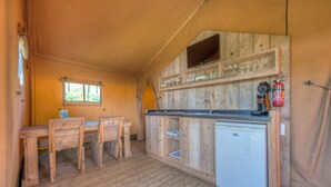 A compact kitchen with wooden cabinets, a small refrigerator, a sink, and a television mounted above the counter. - Forest Glamping near Emmen (Borger)
