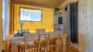 A wooden dining table with chairs, a window with a curtain, and a plant on a shelf.