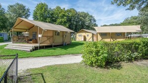 A row of camping tents with wooden decks and benches, surrounded by greenery and trees.