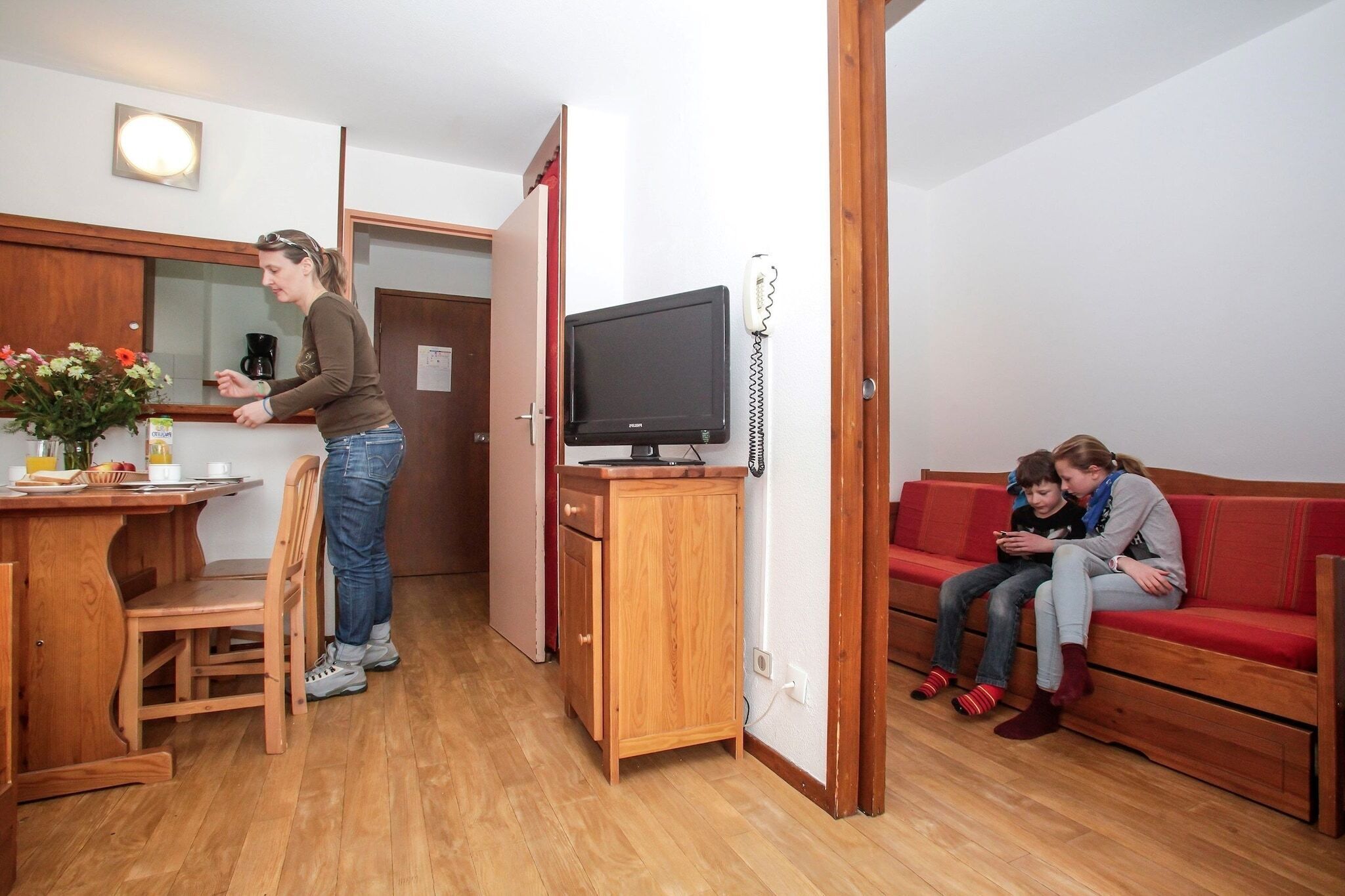 A compact living space with a kitchenette, a wooden cabinet, a television, and a red sofa.