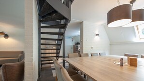 Een moderne eethoek met een houten tafel, stoelen en een trap naar een hoger gelegen niveau.