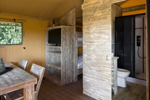 A compact room with a wooden dining table and chairs, a built-in TV shelf, a shower area, and a toilet. - Woodland Glamping Getaway (Borger)