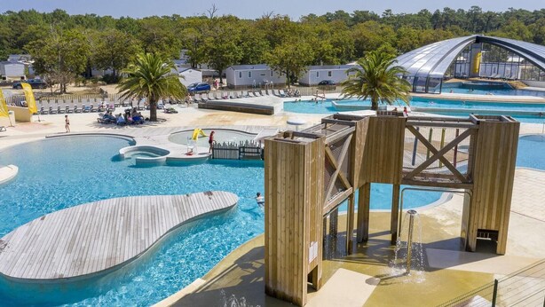 A pool area with multiple swimming pools, wooden deck, and a covered structure.