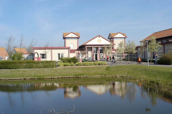 A building with a central entrance, a small pond in front, and a clear sky.