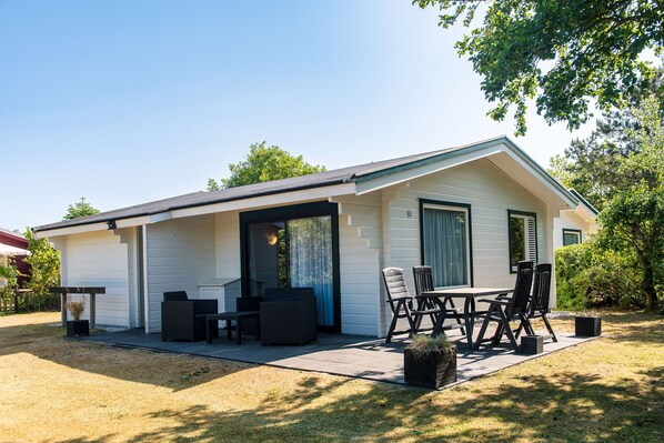 Eingeschossiges Haus mit überdachter Terrasse, komplett mit Tisch und Stühlen.