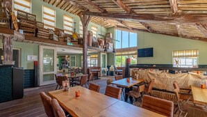 A rustic restaurant with wooden tables and chairs, a wooden ceiling, and a balcony with various items.