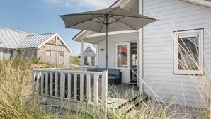 A beachfront house with a covered porch, a wooden deck, and a large umbrella.