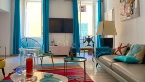 En stue med sofa, fjernsyn, et bord med lampe og et farverigt tæppe.