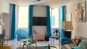 En stue med en loftsvifte, et fjernsyn ophængt på væggen, en sofa, en lænestol, et lille bord og en lampe.