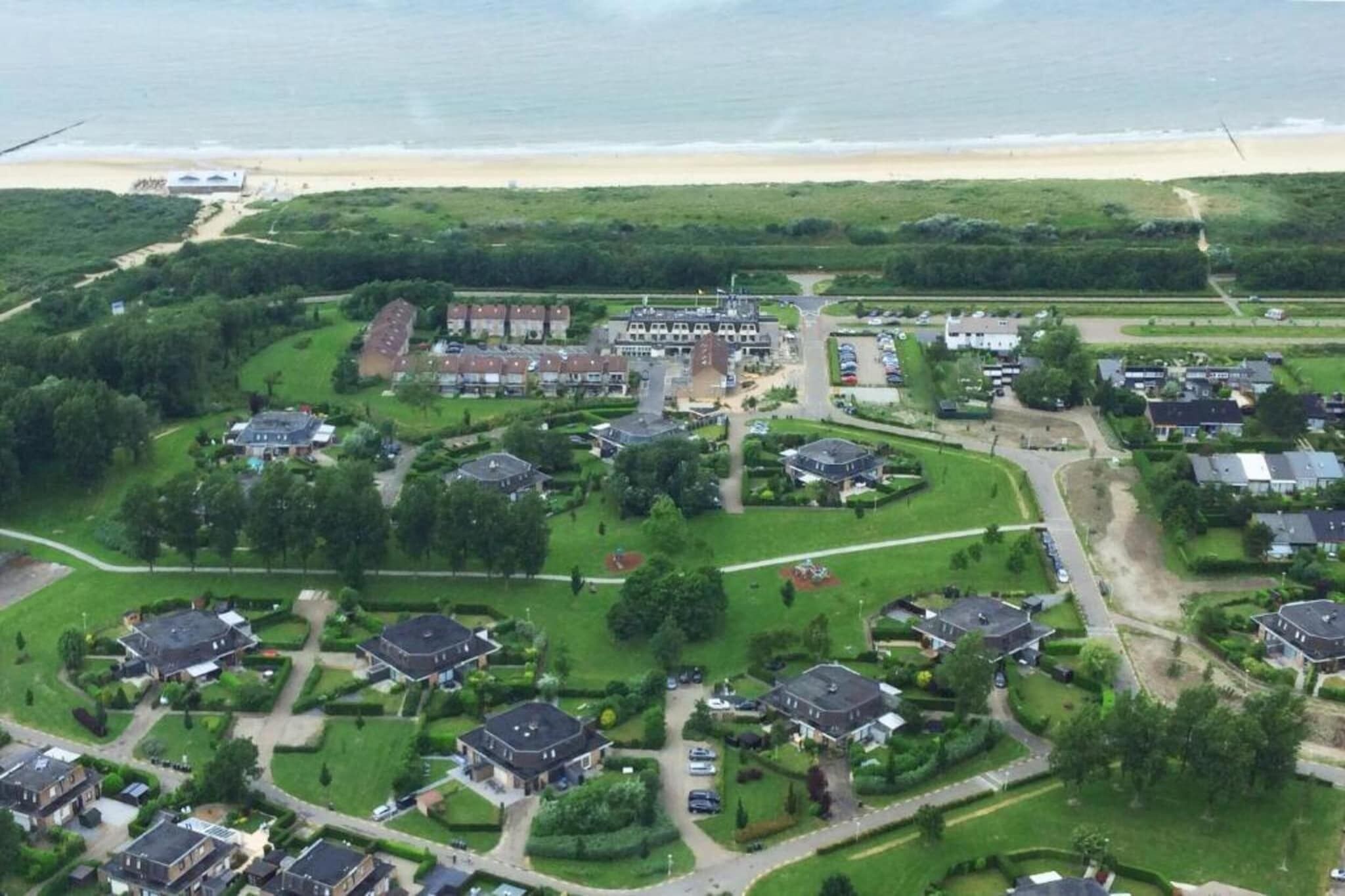 Vue aérienne d’un quartier résidentiel avec des maisons, des pelouses verdoyantes et une plage en arrière-plan.