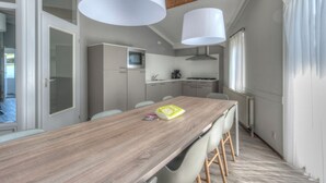 A modern kitchen with a wooden table and chairs, a built-in oven, and a window with curtains. - Bungalow near Dutch Beaches & Nature Trails (Domburg)