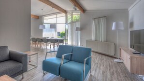 A modern living room with a blue sofa, a grey armchair, and a wooden cabinet. There is a dining area with a table and chairs in the background. - Bungalow near Dutch Beaches & Nature Trails (Domburg)