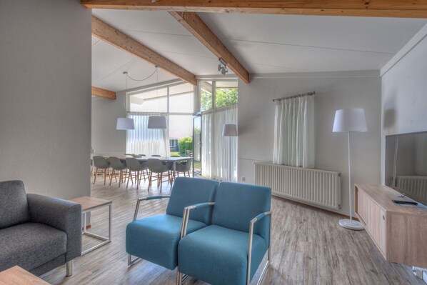 A modern living room with a blue sofa, a grey armchair, and a wooden cabinet. There is a dining area with a table and chairs in the background.