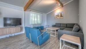 A modern living room with a flat-screen TV, blue and gray sofas, a wooden coffee table, and a painting on the wall. - Bungalow near Dutch Beaches & Nature Trails (Domburg)