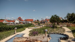 Eine Küstenlandschaft mit einem Sandweg, Holzbauten und Häusern mit roten Dächern.