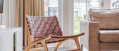Un salon moderne avec un fauteuil en cuir marron, un canapé beige et une grande fenêtre donnant sur des immeubles.