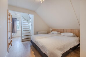 A bedroom with a bed, a wooden headboard, a window with curtains, and a staircase leading to an upper floor. - Villa in Cadzand-Bad near North Sea Beach (Cadzand-Bad)