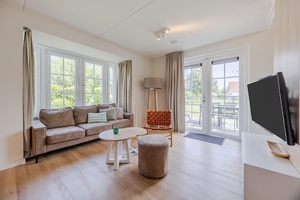 A living room with a sofa, round table, ottoman, chair, lamp, and a TV. - Villa in Cadzand-Bad near North Sea Beach (Cadzand-Bad)