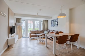 A modern living room with a sofa, dining table, chairs, a TV, and a large window. - Villa in Cadzand-Bad near North Sea Beach (Cadzand-Bad)