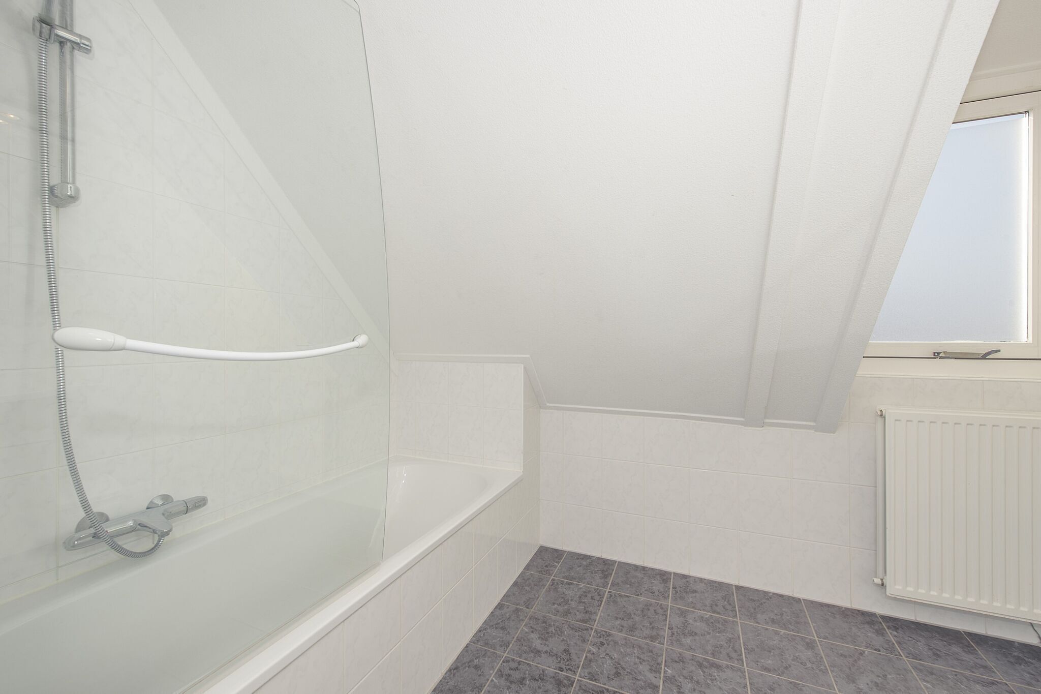 Un baño moderno con ducha de vidrio, una bañera blanca y un ventanal que proporciona luz natural.
