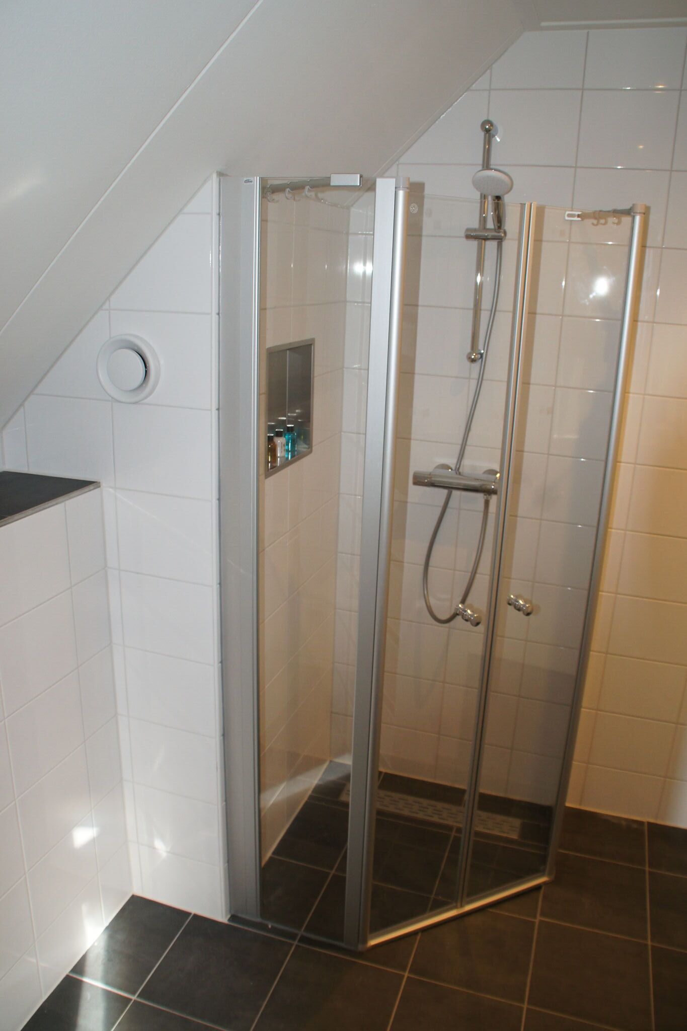 Et brusebad med glasvægge, en håndbruser og et kontrolpanel på væggen.