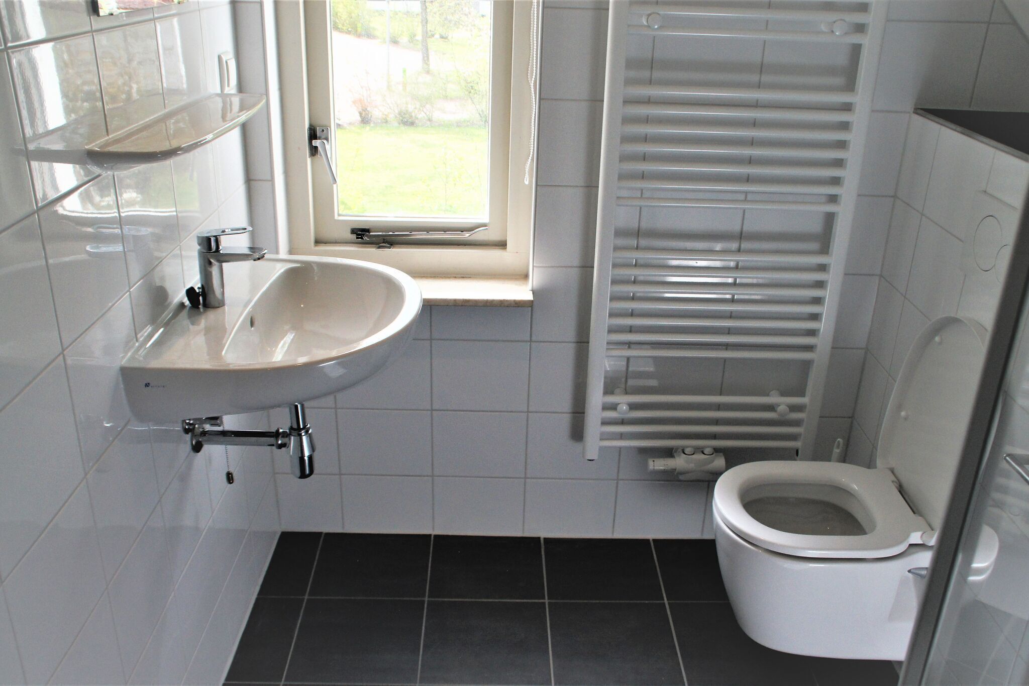 Et badeværelse med en hvid vask, toilet og et vindue.