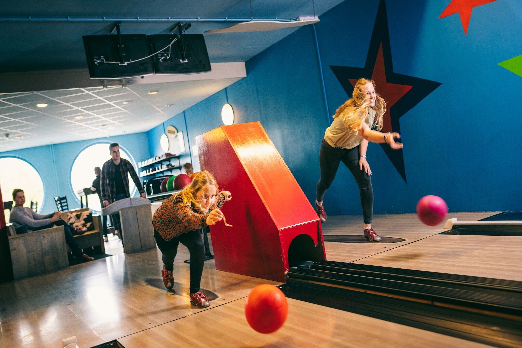 A bowling alley with a large star mural on the wall, a red bowling pin, and a bowling ball in motion.