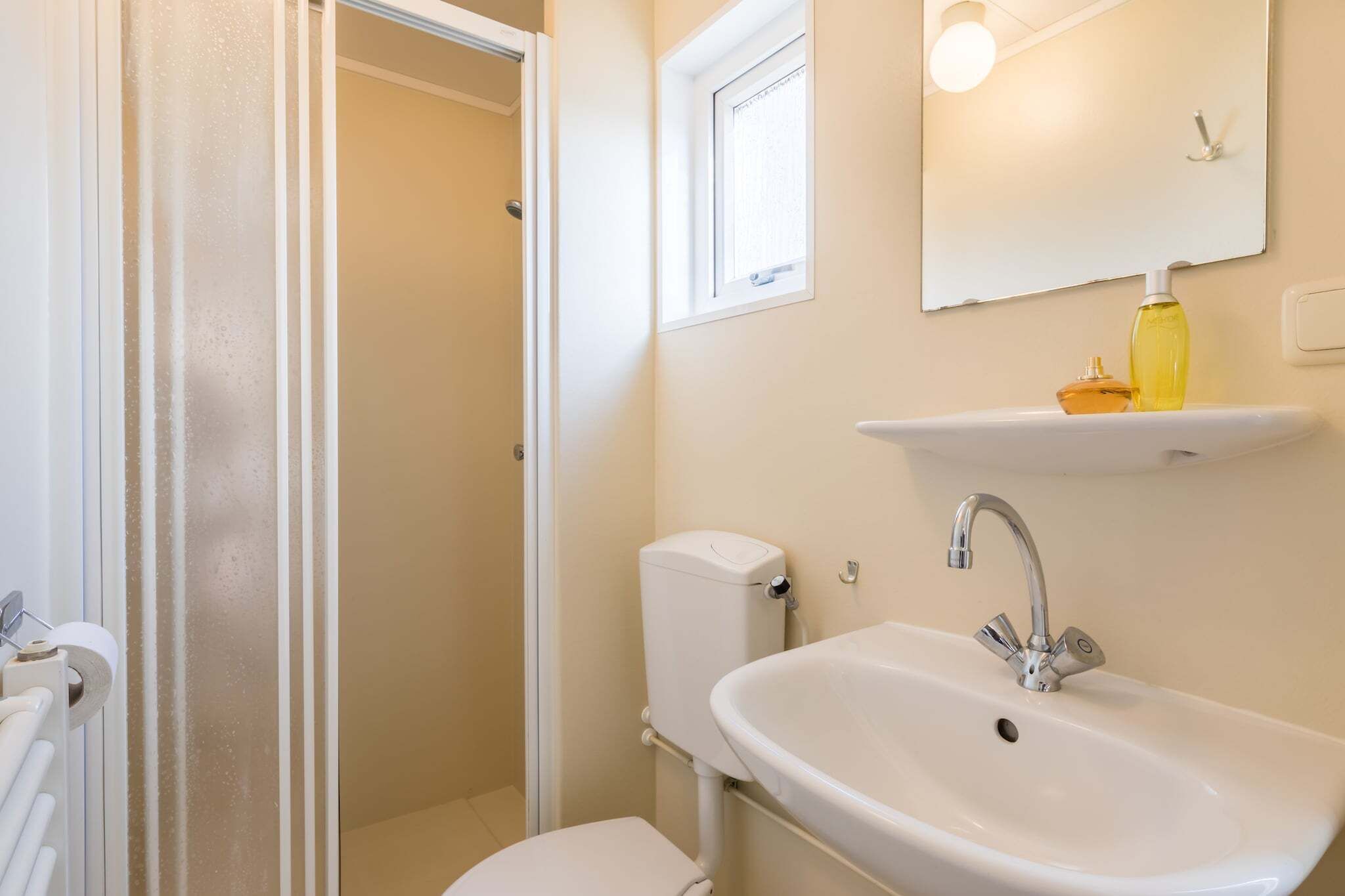 A bathroom with a toilet, sink, and a window above the mirror.