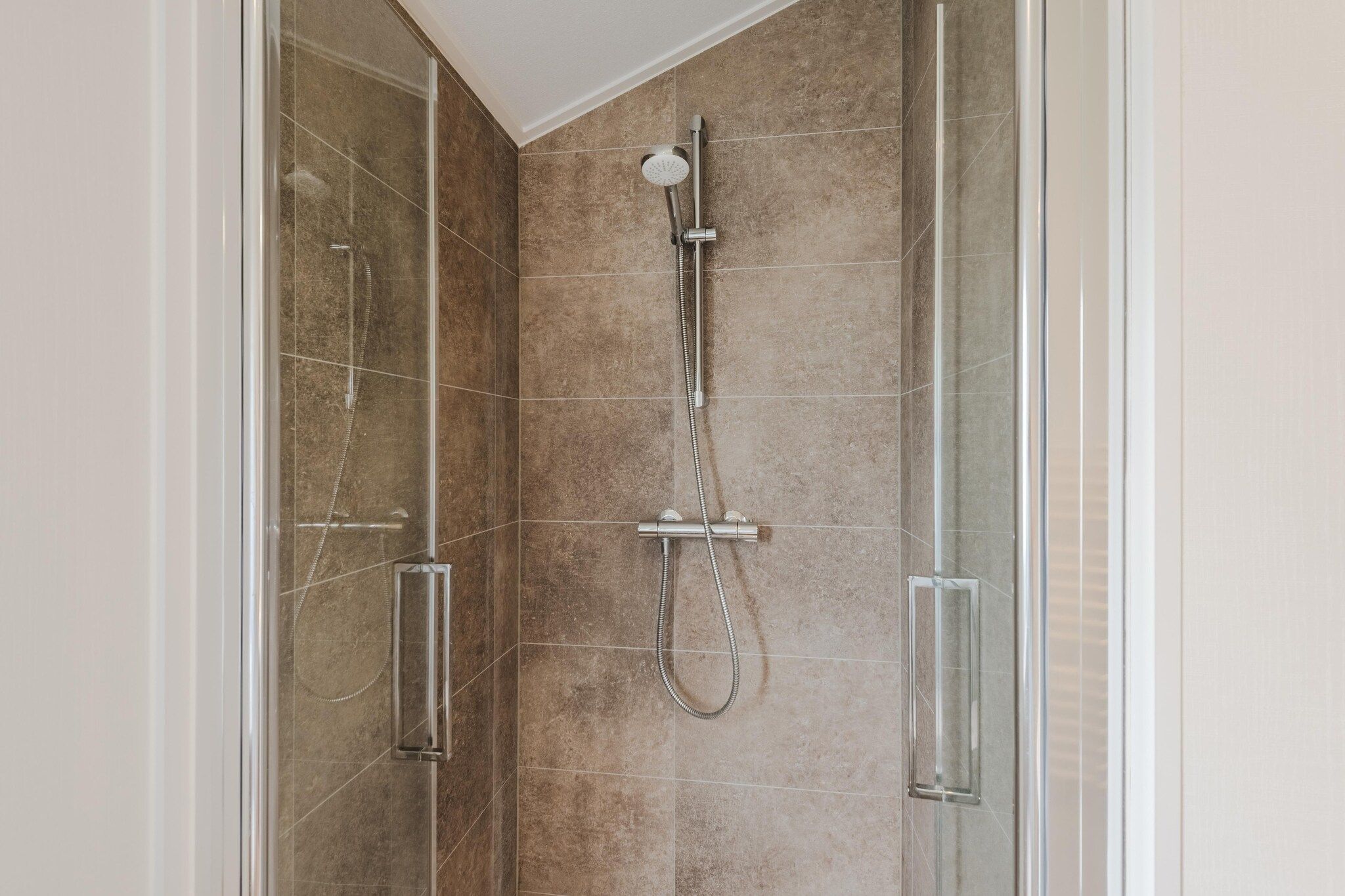 Een douche met glazen wand, een handdouche en een kraan op de muur.