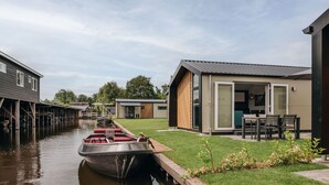 Une propriété située au bord d’un canal, dotée d’un quai pour bateaux, d’une allée couverte et d’une maison moderne avec une porte en verre.