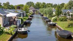 Un canal bordé de bateaux, une rangée de maisons d’un côté et une zone herbeuse parsemée de fleurs.