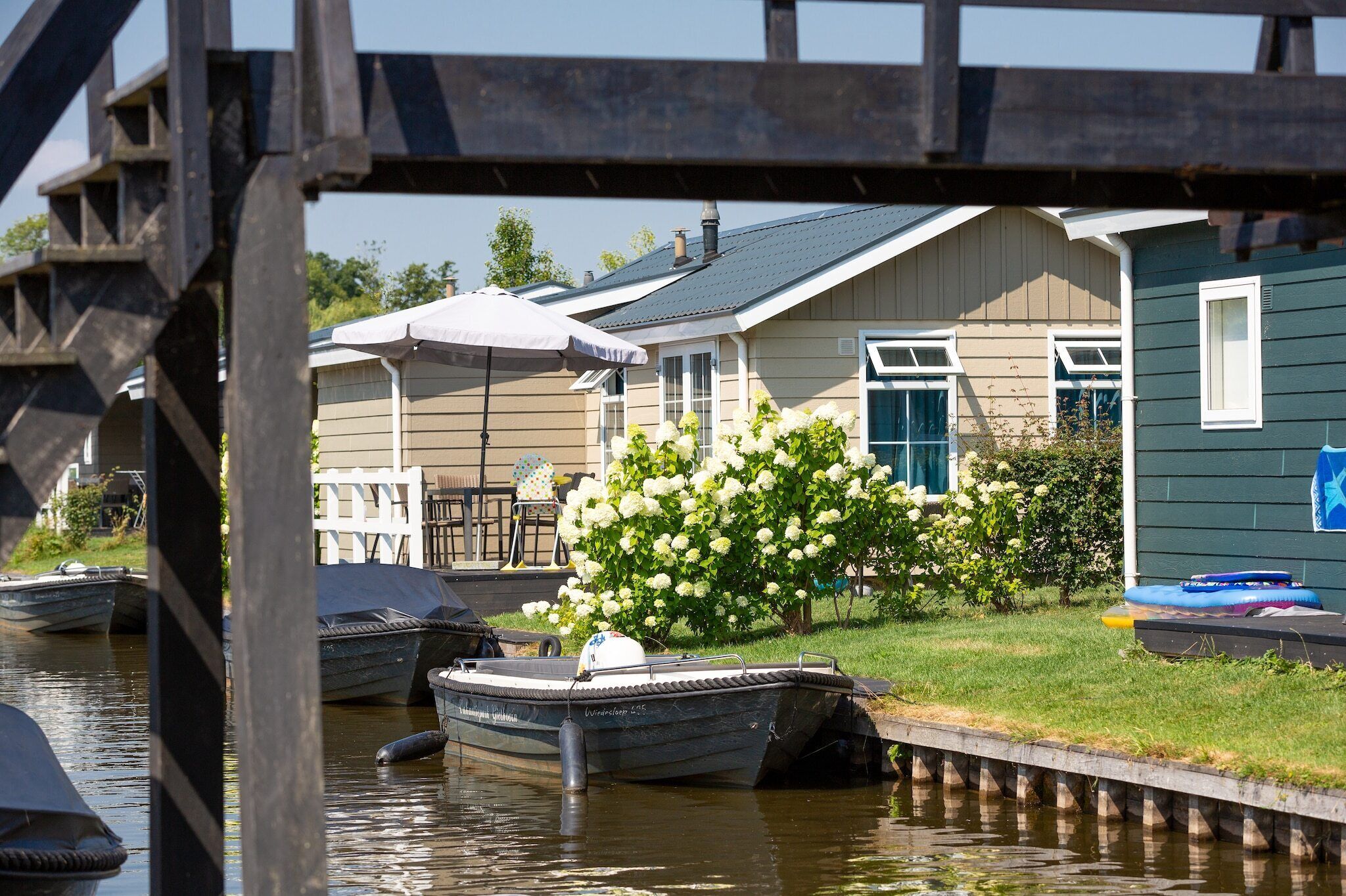 A houseboat docked at a pier with a small garden and a white flower bush.
